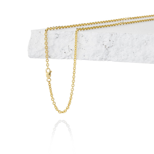 A delicate gold chain necklace draped over a white textured stone block on a clean white background.