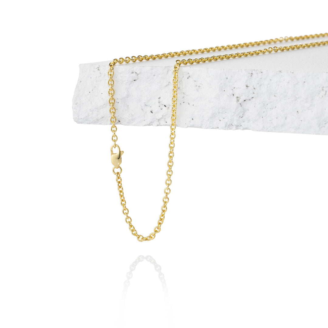 A delicate gold chain necklace draped over a white textured stone block on a clean white background.