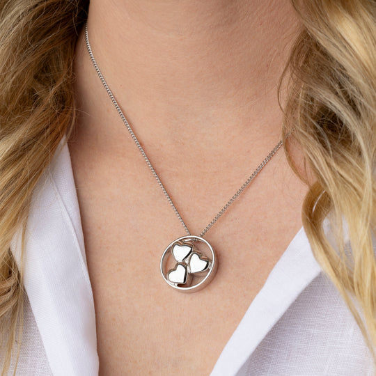 Silver necklace with a circular pendant worn by a person in a white shirt.
