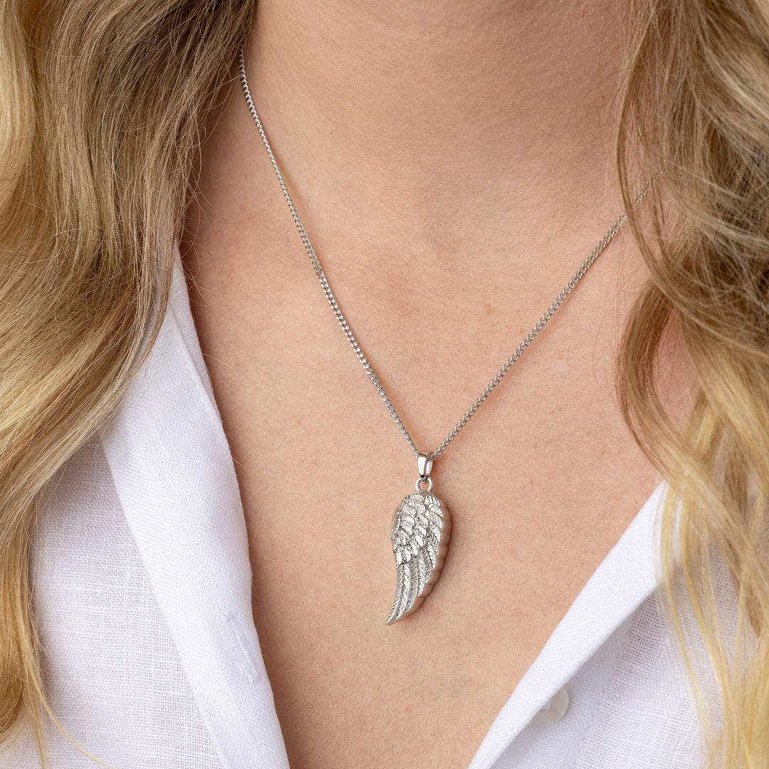 Silver angel wing necklace worn by a person with blonde hair and a white shirt.