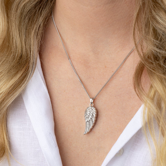 Silver angel wing necklace worn by a person with blonde hair and a white shirt.