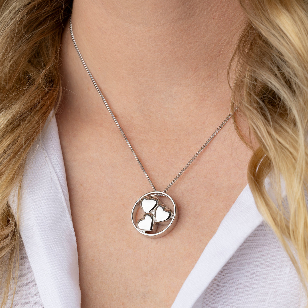 Silver necklace with a circular pendant worn by a person in a white shirt.