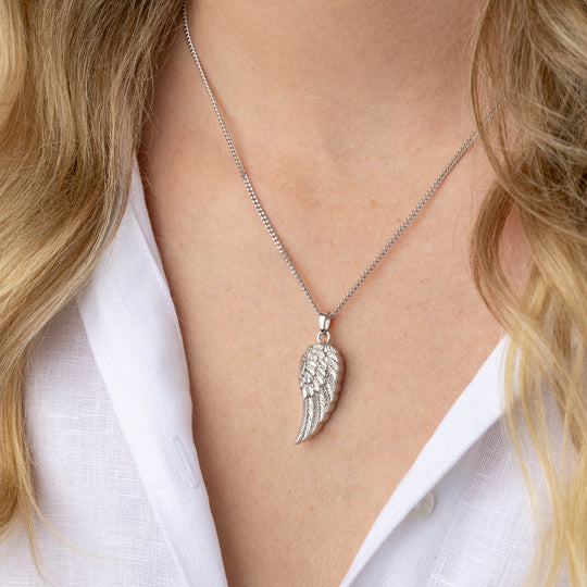 Silver angel wing necklace worn by a person with blonde hair and a white shirt.