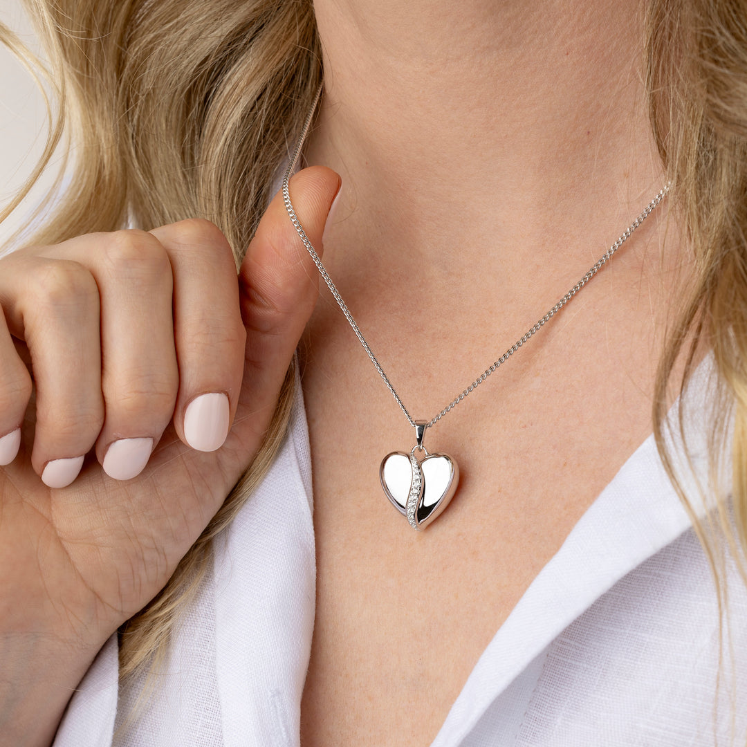 A close-up of a model wearing a silver split-heart pendant necklace, styled with a white collared shirt.
