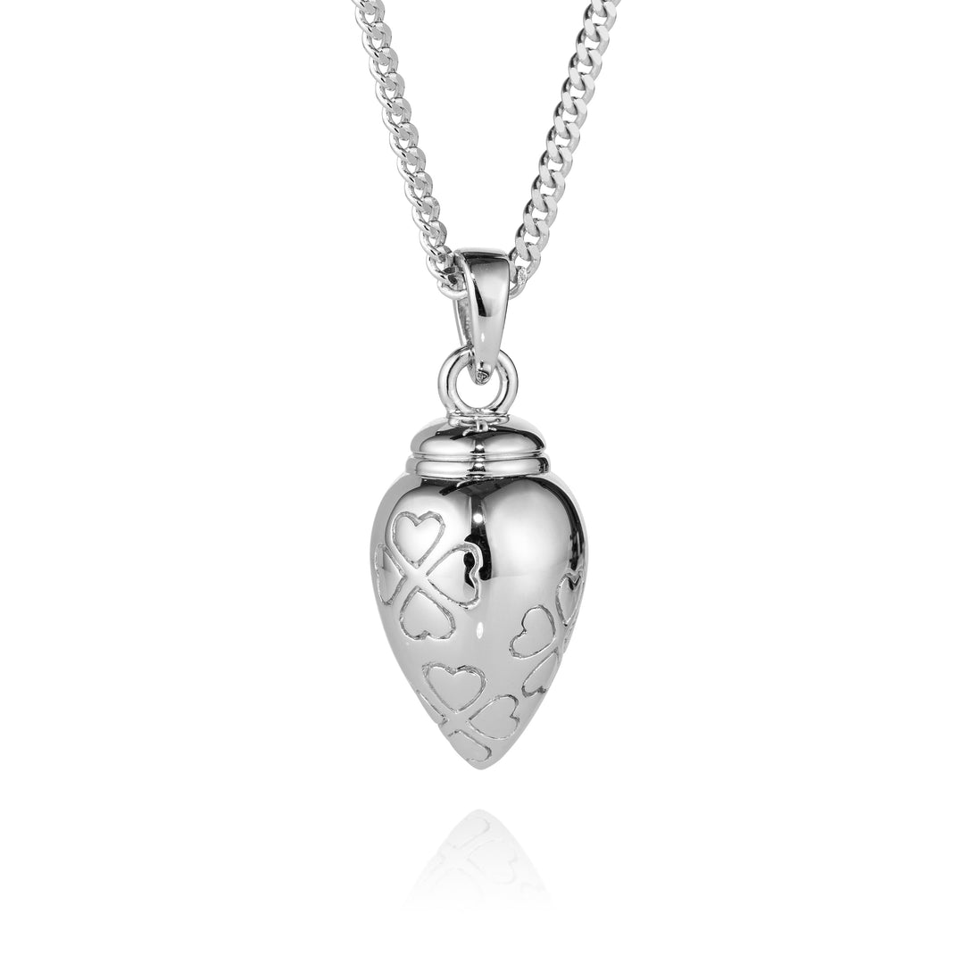 A silver heart-shaped urn pendant necklace with engraved hearts and a heart-shaped ribbon motif, hanging from a silver chain on a white background.