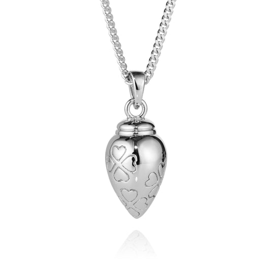 A silver heart-shaped urn pendant necklace with engraved hearts and a heart-shaped ribbon motif, hanging from a silver chain on a white background.