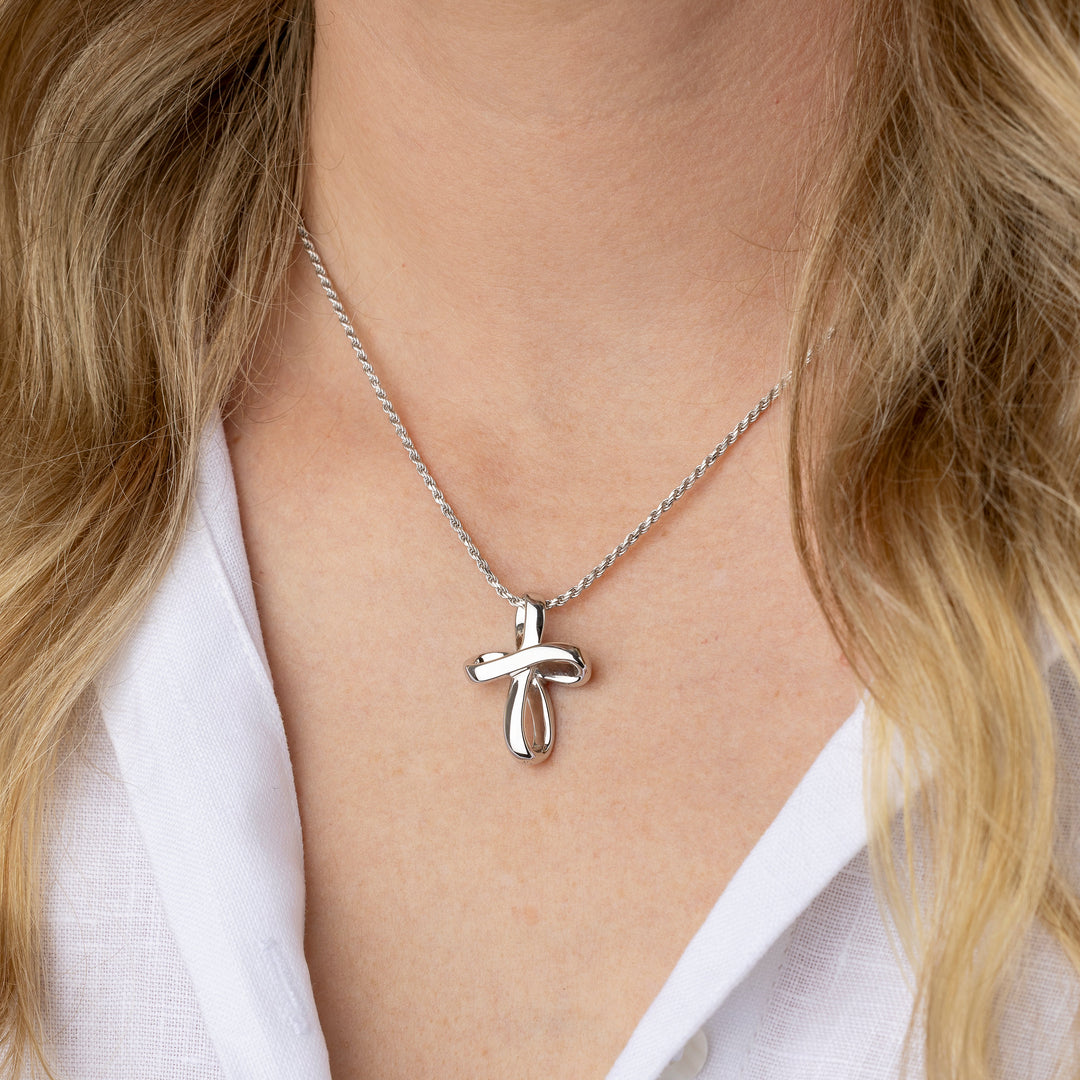 A close-up of a person wearing a delicate silver cross pendant necklace on a fine chain, styled with a white collared shirt.