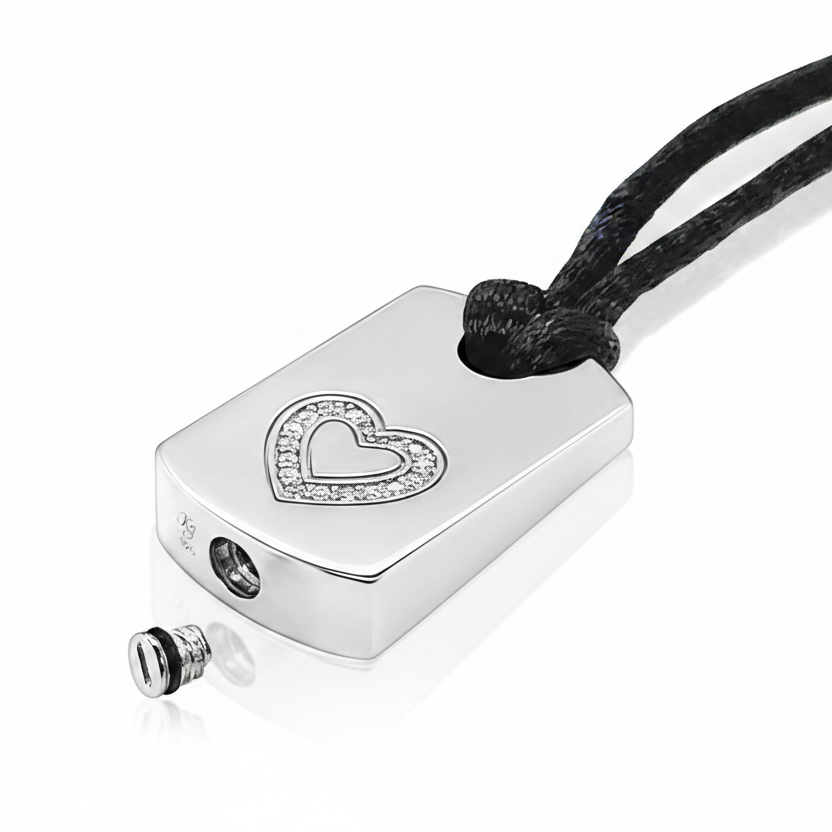 A silver rectangular pendant necklace with a heart-shaped crystal border, attached to a black cord, shown on a white background with a small detached screw detail below.