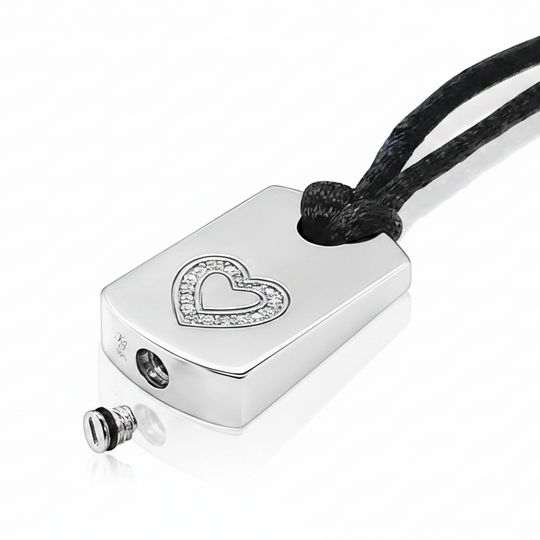 A silver rectangular pendant necklace with a heart-shaped crystal border, attached to a black cord, shown on a white background with a small detached screw detail below.