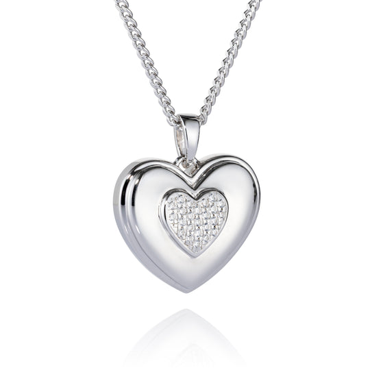 A silver heart-shaped pendant necklace with a polished outer heart and a pavé-set heart in the center, suspended from a silver chain on a white background with a soft reflection below.
