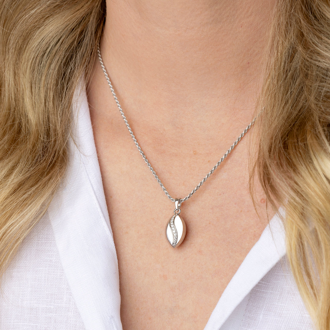 A close-up of a woman wearing a delicate silver chain necklace with a polished silver pendant, styled with a white linen shirt.