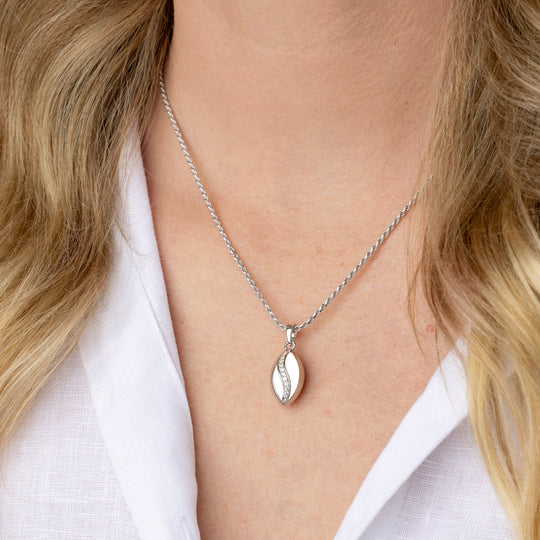 A close-up of a woman wearing a delicate silver chain necklace with a polished silver pendant, styled with a white linen shirt.