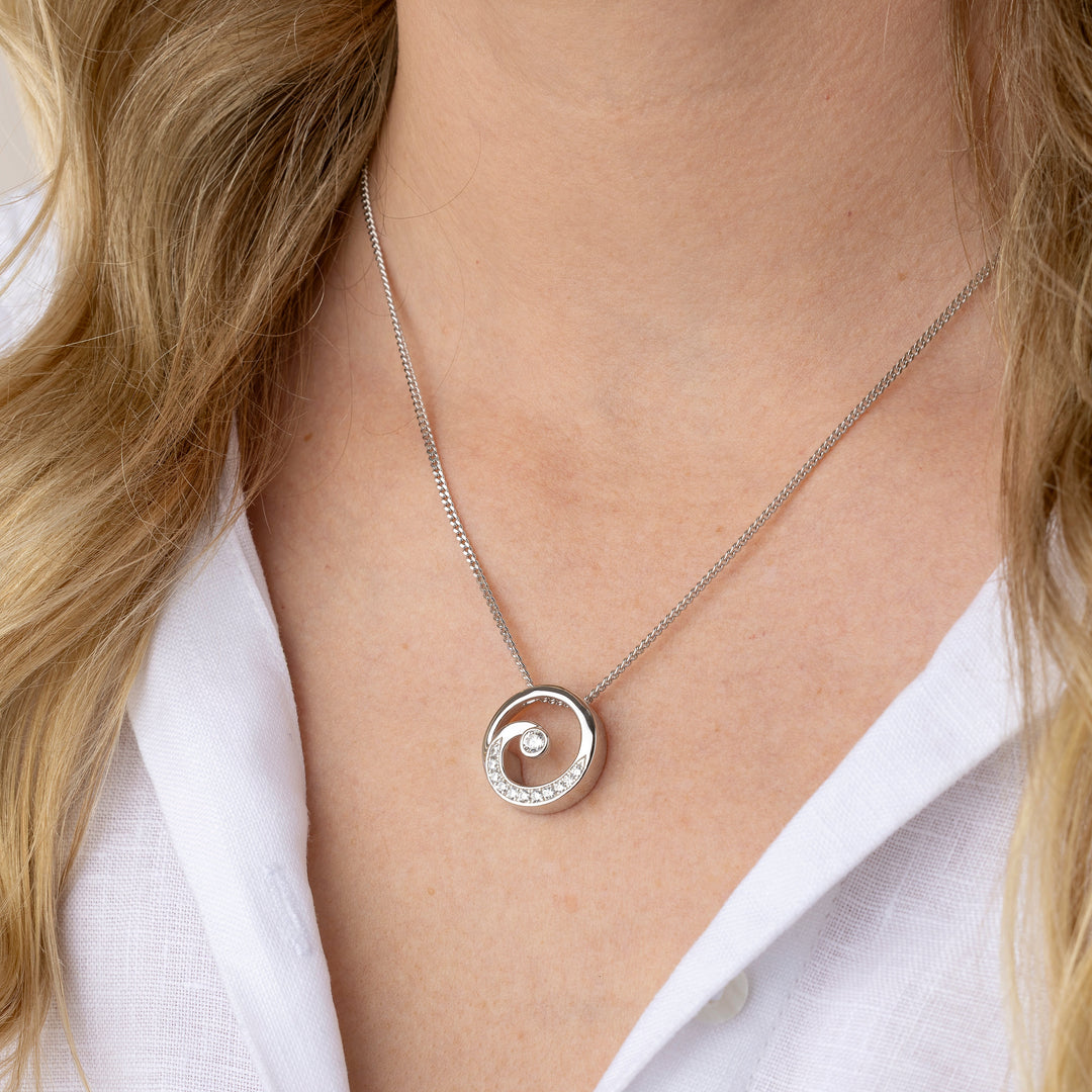 A close-up of a model wearing a silver spiral pendant necklace with a white collar.