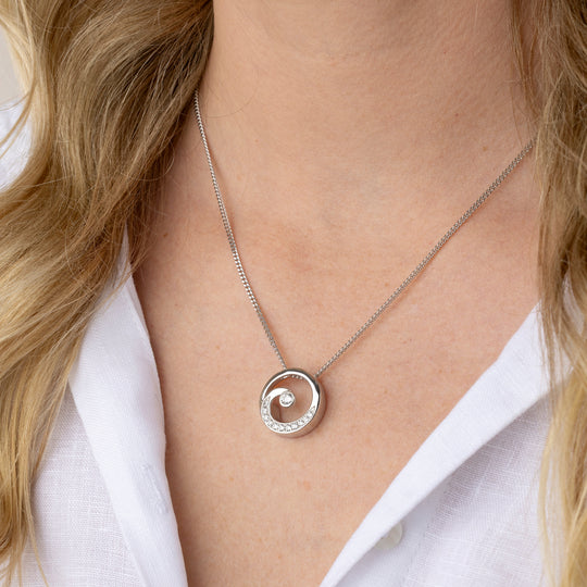 A close-up of a model wearing a silver spiral pendant necklace with a white collar.